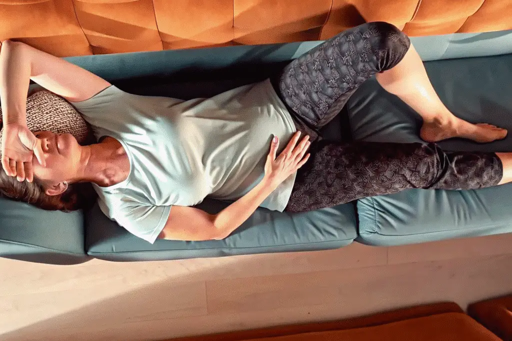 Woman resting on a couch holding her stomach due to discomfort, possibly related to fibermaxxing effects.